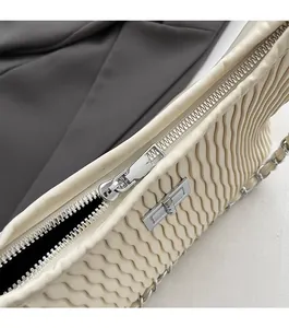 Detail of beige pleated shoulder bag featuring smooth silver zipper and metal twist lock