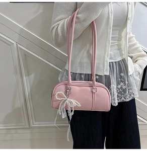Detail of pink faux leather Boston bag with pearl bow and lace ribbons on a white wall