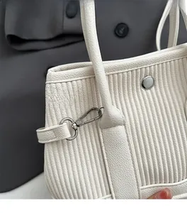 Close-up of white pleated bucket bag with silver metal lock and litchi texture finish