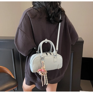 Close-up of a blue Boston bag with dual handles, silver zippers and a cute plush charm