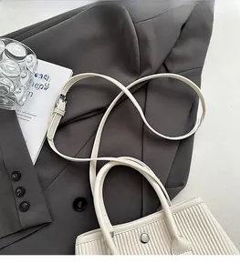Detailed view of white vertical textured bucket bag featuring silver hardware on gray suit
