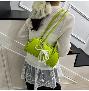 Green cylindrical shoulder bag with lace bow and pearl charm on a female model