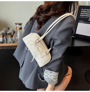 Close-up of cream shoulder bag featuring elegant pearl lace bow and textured leather