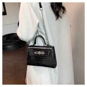 Rear view of model holding a black crocodile pattern trapezoid bag with silver chain strap