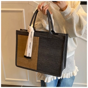 Detail shot of a large two-tone canvas tote bag with decorative printed ribbon accessory