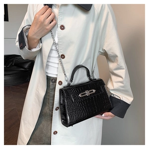 Detail of black crocodile texture bag with silver twist lock on light trench coat