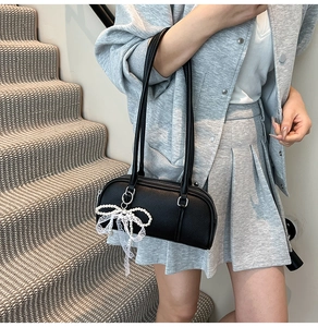 Detail of black litchi grain leather Boston bag with a white lace bow pearl charm