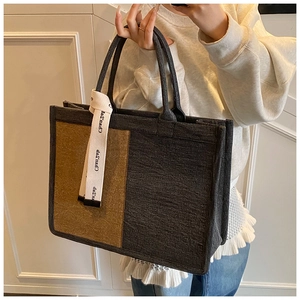 Detail view of a two-tone tweed tote bag with decorative brand ribbon and sturdy handles