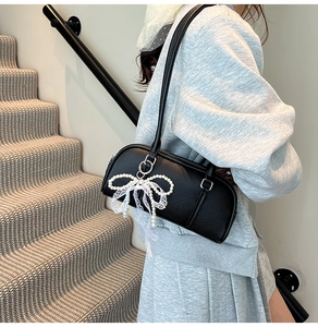 Detail of black cylinder bag with large lace bow and pearl accents on shoulder strap