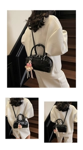Detail of glossy black Boston bag with dual handles and plush charm on the shoulder strap