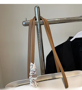 Detail of cream tote bag featuring brown leather strap and decorative floral silk scarf
