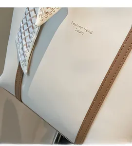 Close-up of cream leather tote bag featuring a brown strap and patterned silk scarf detail