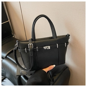 Détail d'un sac cabas en cuir grainé noir avec fermoir rotatif argenté sur un canapé