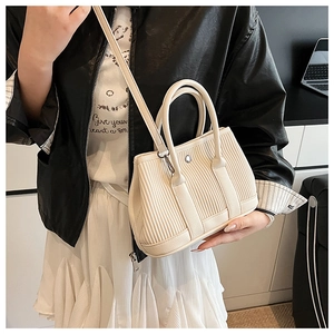 Detail showing creamy white pleated bucket bag with dual handles and metal D-ring attachment