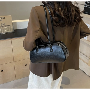 Side view of a vintage pleated black leather shoulder bag styled with a brown blazer