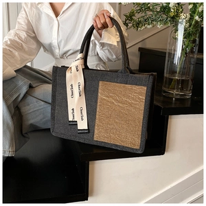 Detail of grey felt tote bag with brown patch and a decorative branded ribbon on handle