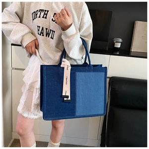 Detail of color-block denim tote bag featuring blue fabric patchwork and canvas handle