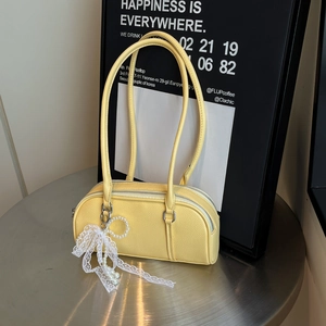 Elegant pale yellow Boston bag with a vintage pearl pendant on a sleek metal table