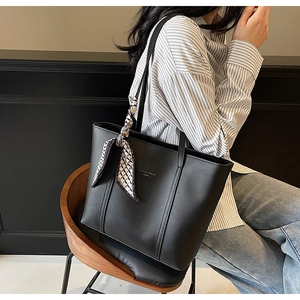 Detail of black faux leather tote bag with fashion text print and plaid silk scarf decoration