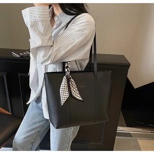 Black leather tote bag with silk scarf detail worn by model in a minimalist room