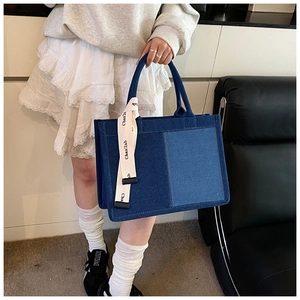 Detail of a large color-block denim tote bag with printed ribbon on a female model