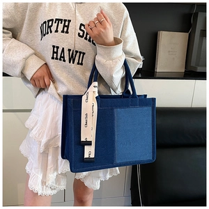 Detail of blue denim tote bag with contrast stitching and branded canvas strap