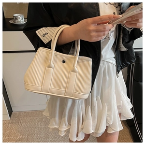 Detail of off-white pleated tote bag showing vertical textures and silver metal buckle