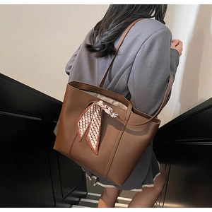 Detail of a brown leather tote bag with a red and white checkered scarf on the handle