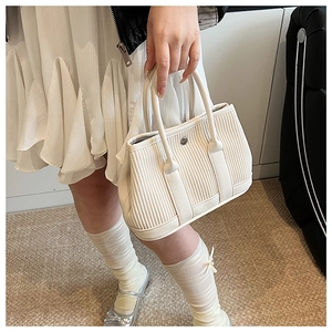 Close-up of pleated beige tote bag showing vertical textures and silver metal snap button