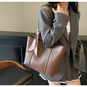 Detail of a large brown tote bag with textured finish and decorative printed silk scarf
