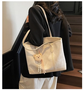 Detail of white tote bag with a small brown teddy bear charm and textured PU leather finish