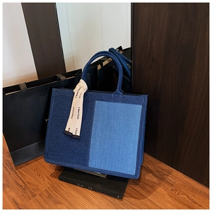Detail of blue patchwork denim tote bag with decorative beige printed handle ribbon