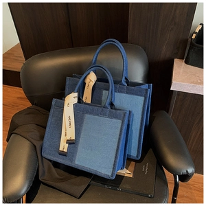 Detail of blue patchwork denim tote bags in two sizes on a black leather chair