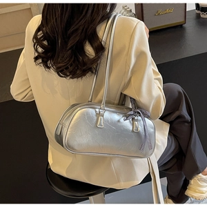 Silver ballet-style shoulder bag with a checkered bow detail shown on model's shoulder