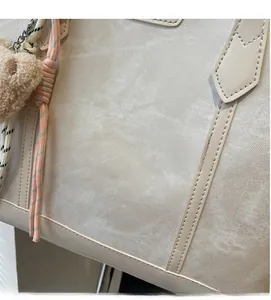 Detail of off-white fabric tote bag with leather straps, chain, and cute bear charm