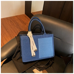 Detail of color-block denim tote bag showing blue fabric stitching and logo ribbon strap