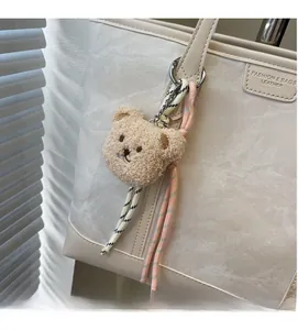 Detail of light brown plush bear charm with woven ropes on a white leather tote bag