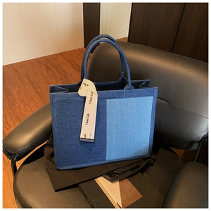 Close-up of patchwork denim tote bag with decorative beige ribbon on black leather chair