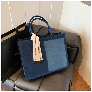 Detail of blue patchwork denim tote bag with decorative beige ribbon on leather sofa