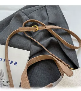 Detail of adjustable beige leather shoulder strap with gold metal buckle on a bucket bag