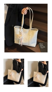Detail view of cream tote bag with thin shoulder straps and a plush bear pendant charm