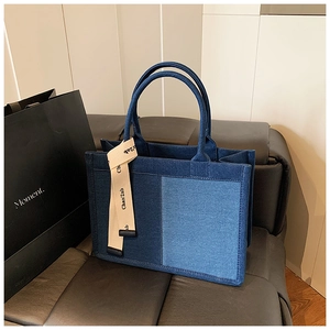 Detail of blue denim tote bag with patchwork design and logo webbing on handles