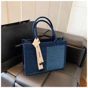 Detail of navy canvas tote bag featuring light blue patch and beige lettered strap on leather