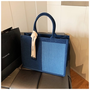 Detail of a color-block denim tote bag with navy and light blue patchwork and strap