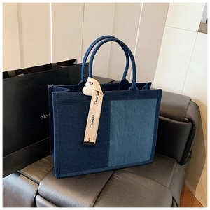 Detailed view of bicolor denim tote bag with decorative logo strap on leather seat