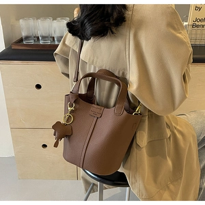 Close-up of brown litchi pattern bucket bag with an elephant charm on a model