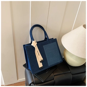 Detail view of denim patchwork tote bag with ribbon decoration on a leather stool