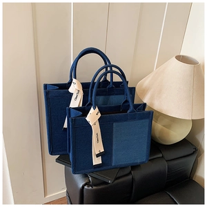 Detail of two denim canvas tote bags in deep blue with stylish white letter print ribbons