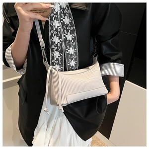 Close-up of beige shoulder bag with vertical pleated texture and leather fringe details