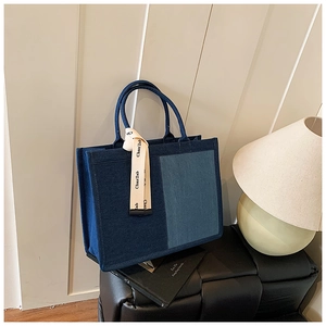 Detail of minimalist denim tote bag with decorative cream ribbon on black woven stool